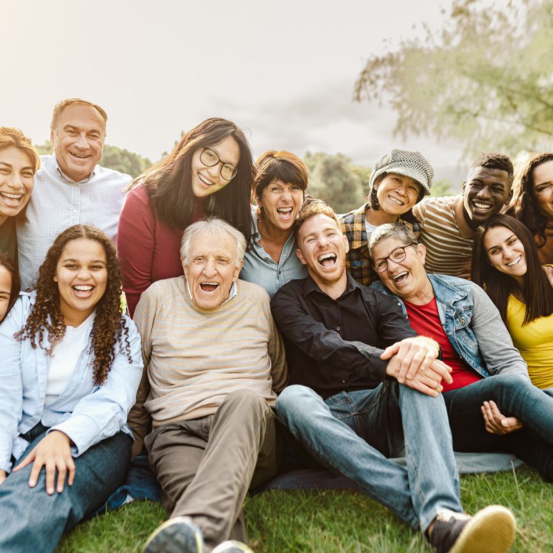 Happy multigenerational people having fun sitting on grass in a public park - People diversity concept